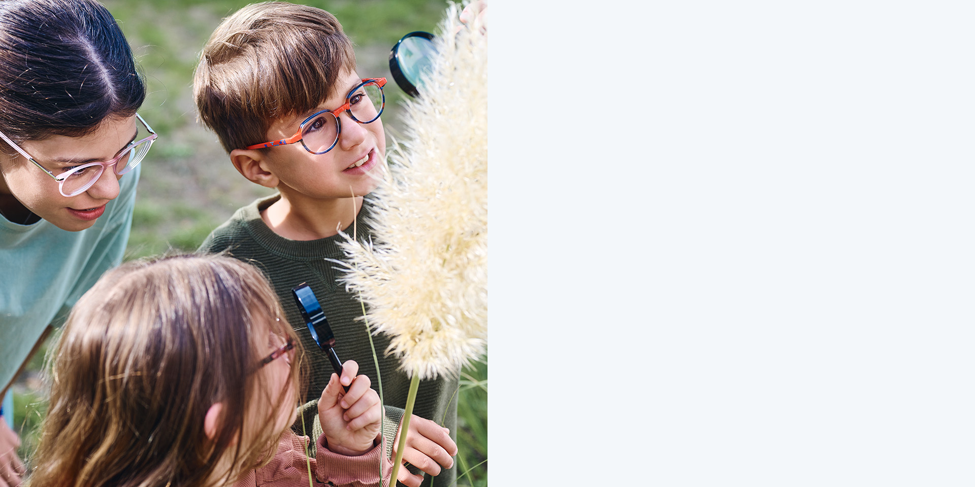 Zwei Mädchen und ein Junge mit ZEISS MyoCare Brillengläsern. Sie sehen sich eine Pflanze an, zwei der drei Kinder betrachten die Pflanze durch Lupen.