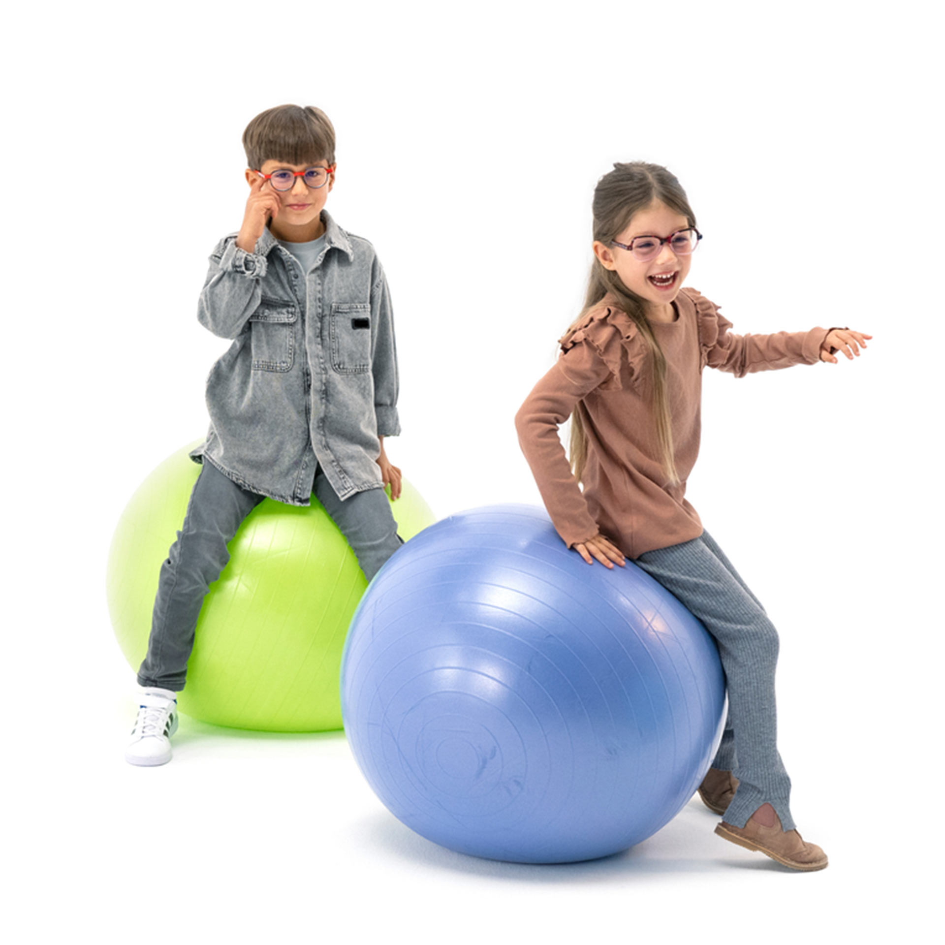 Ein Junge und ein Mädchen, beide mit Brille, hüpfen spielerisch mit Gymnastikbällen herum.