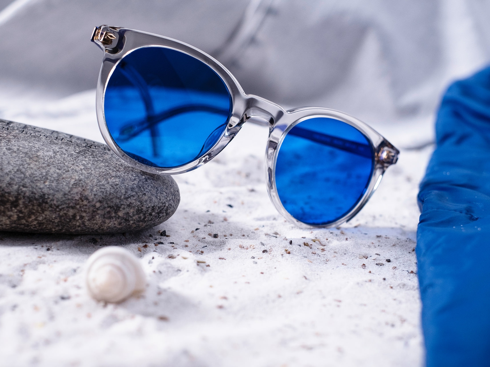 Abbildung einer Sonnenbrille mit blauer Tönung, die halb auf einem Stein liegt
